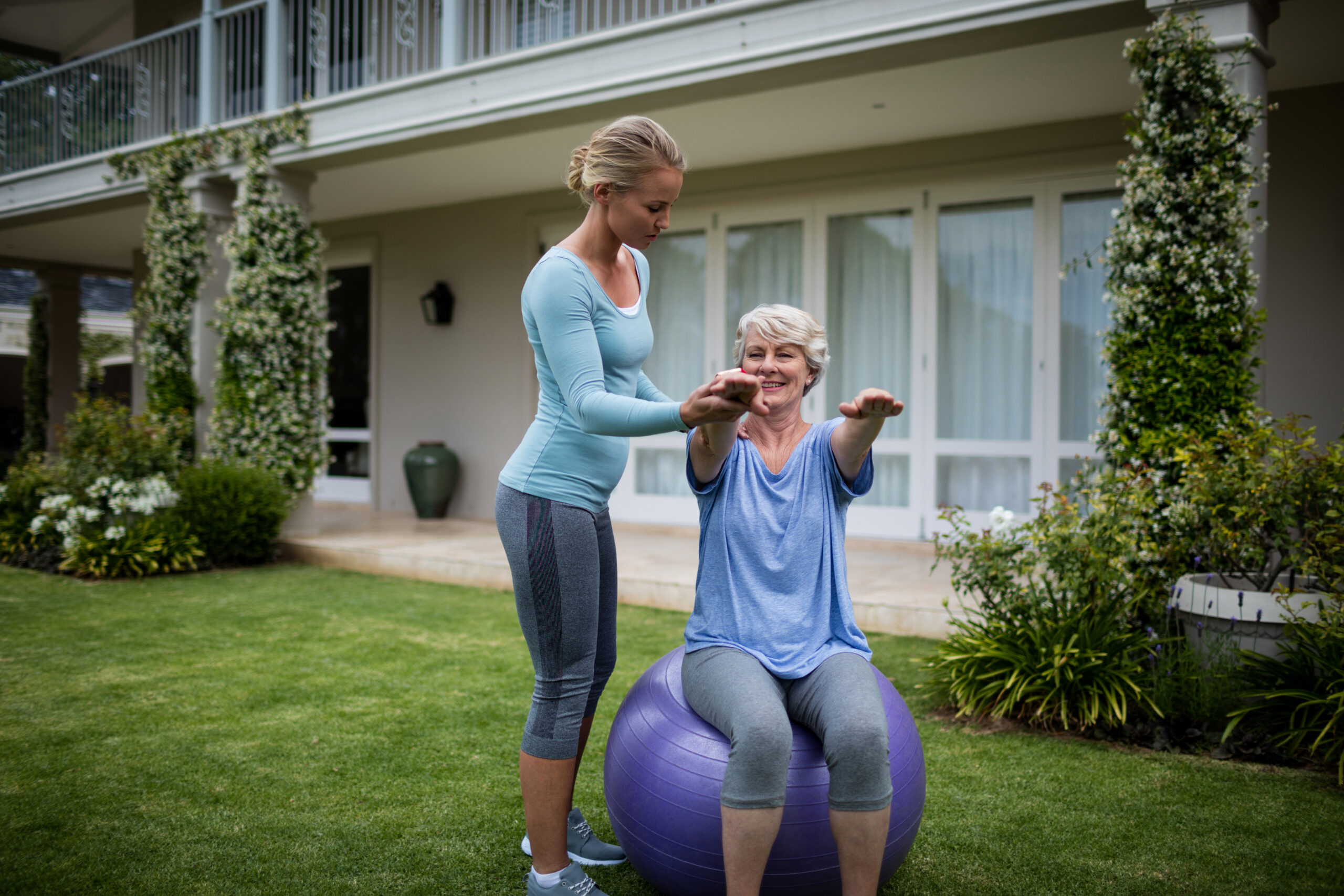 Female coach assisting senior woman in performing exercise in lawn